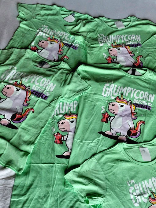 Sechs, übereinander liegende Shirts mit grummelig schauendem Einhorn und der Aufschrift "I'm Grumpycorn before my coffee"