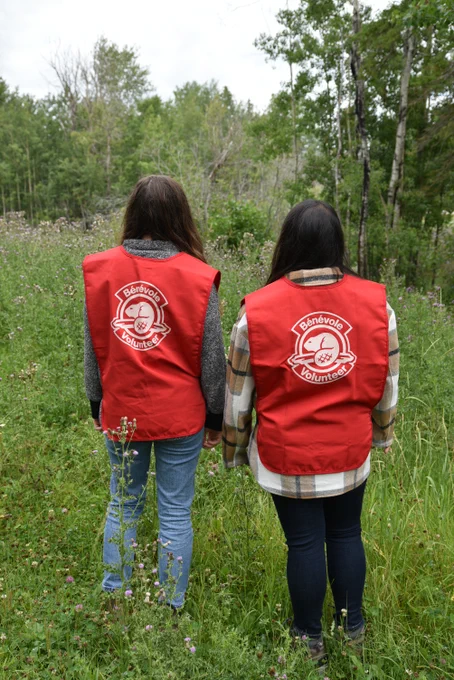 Two community scientists wear red volunteer vests while conducting surveys at Elk Island National Park.