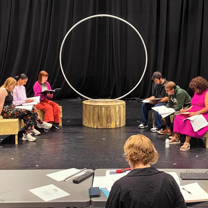 ID Our wonderful cast of five sit on crescent benches on the stage at CAPA College with director Cheryl Martin for their first read through.