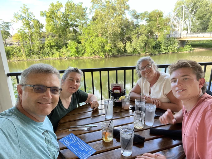 Four people sit at a dinner table under a gazebo at river's edge in Fort Wayne, IN