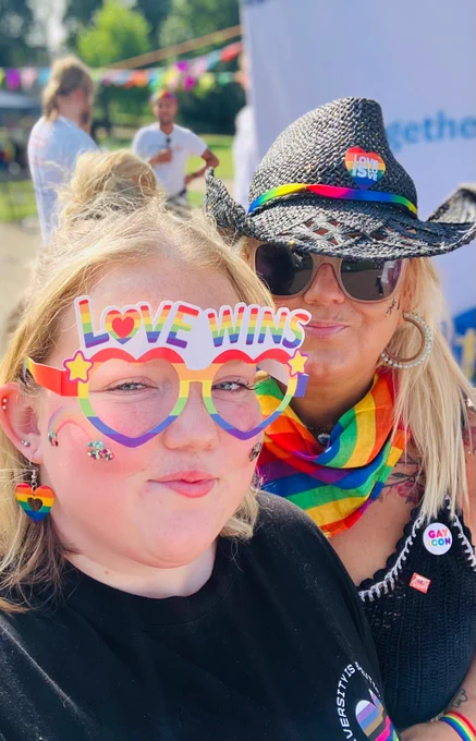 Two people posing for a selfie at Warwickshire Pride 2024, wearing Pride accessories such as glasses that say 'Love Wins'. 