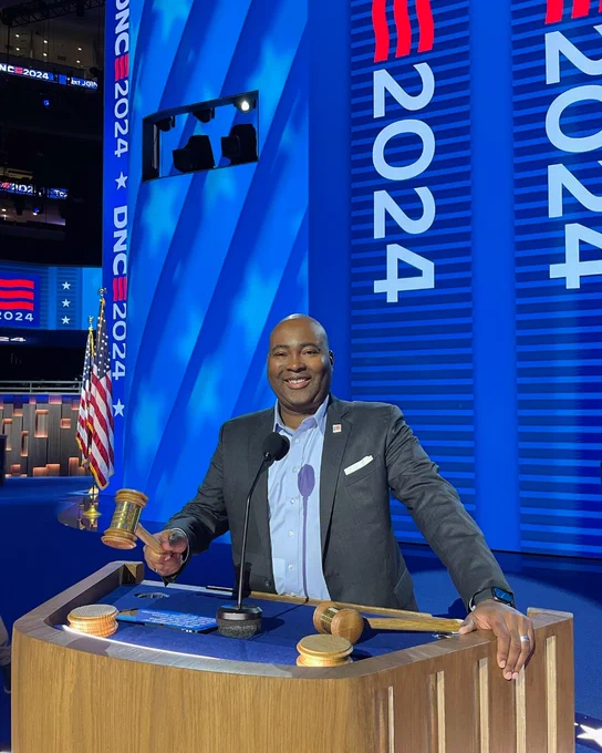 DNC Chair Jaime Harrison holding the gavel and standing at the DNC Convention podium. 