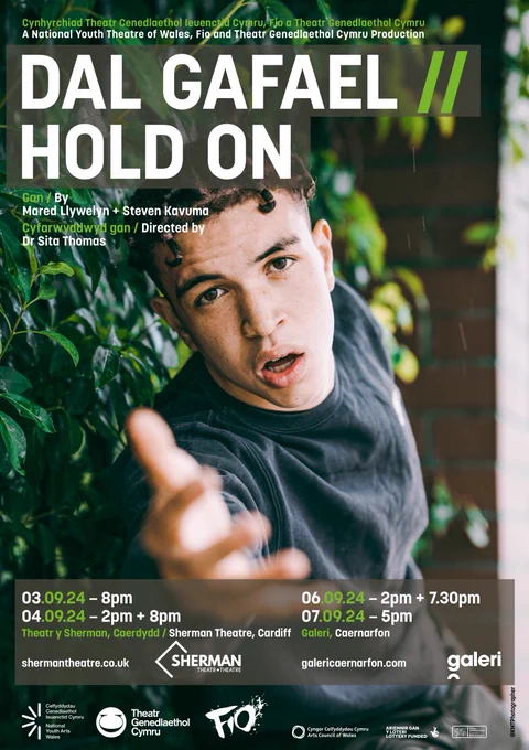 Poster promoting the new show Dal Gafael/Hold On. A person stands in front of greenery, with their arm reaching forwards towards the camera.