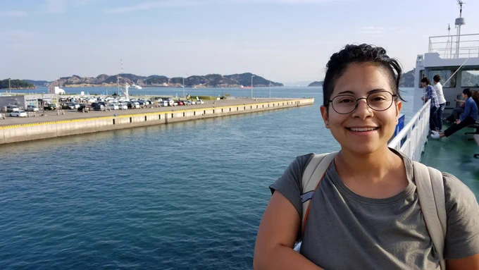 Audrey smiling for the camera on the deck of a boat with a harbor and mountains behind her