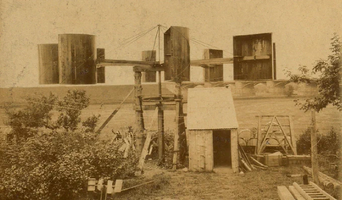  A 19th century windmill with semi cylindrical boxes attached to four strong arms at the bottom of a garden. 