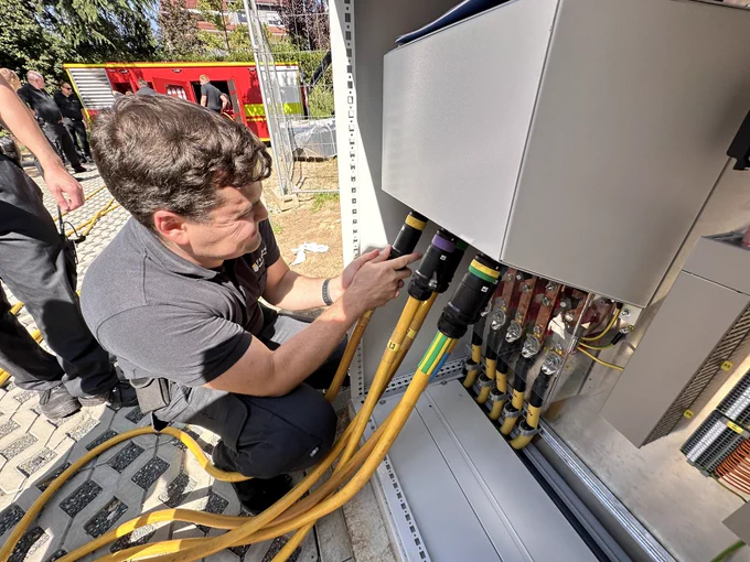 Ein Feuerwehrmann schließt die Kabel des Abrollbehälters Netzersatzanlage an den Neubau der Albin-Göhring-Halle in Bad Homburg-Ober-Eschbach an.