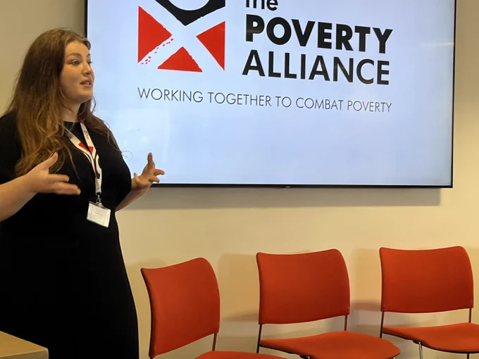 Lydia speaking in in front of a poverty alliance logo