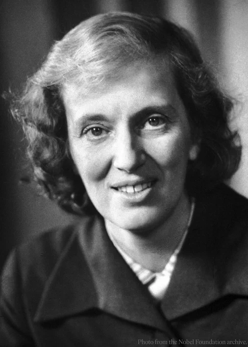 Black and white portrait of Dorothy Hodgkin, smiling slightly, wearing a coat and blouse. 