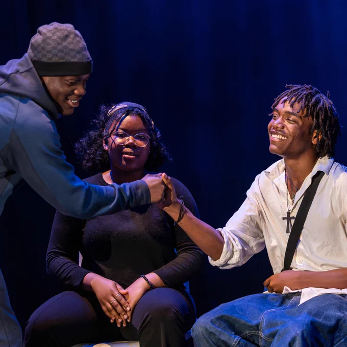 Two smiling young men clasp hands while a young woman watches on.