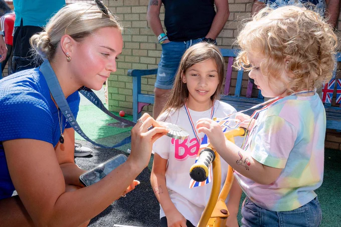 Kate is showing her silver medal to two young children.