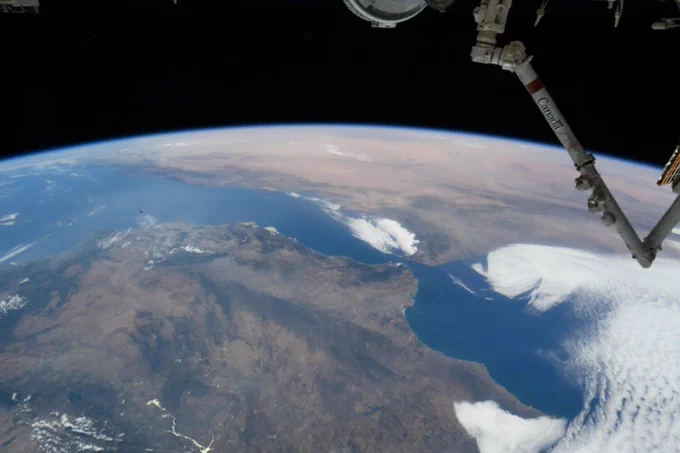 An image of Earth, as seen from the International Space Station. Our home planet's curvature arcs over the top of the photo, with large landmasses and blue seas visible below. The station's Canadarm2 is visible on the right side of the photo. Credit: NASA