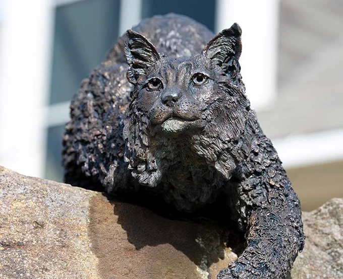 Bronze sculpture of a lynx perched on rocky terrain.