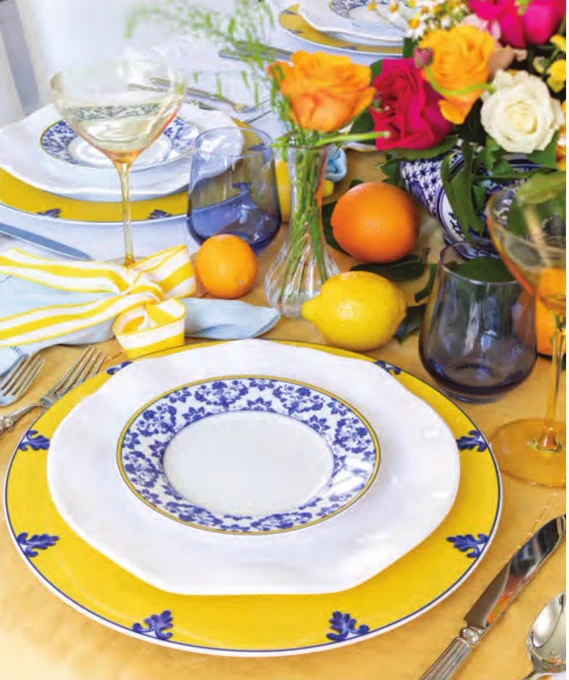 Second: A vivid Mediterranean-inspired place setting with blue, white, and yellow Vista Allegre dishes; yellow and blue glassware from Estelle Colored Glass; and an orange and pink flower arrangement surrounded by lemons and oranges. 

