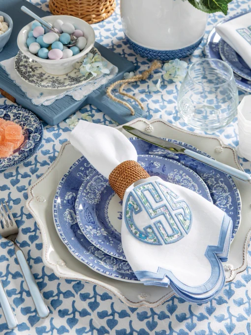 Third: A place setting in a baby blue and white palette with Spode Camilla dishes, a white scalloped Juliska charger, Azzurro Fantasia enameled flatware, and a napkin appliqued with a Liberty London floral print monogram. 