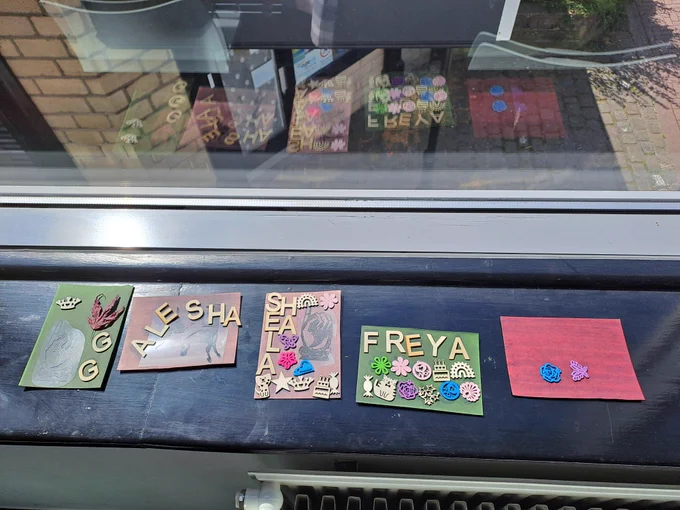5 sheets of pre-treated paper used for cyanotyping on a windowsill in the sunshine. Each sheet has different craft materials such as letters and animals placed in different ways