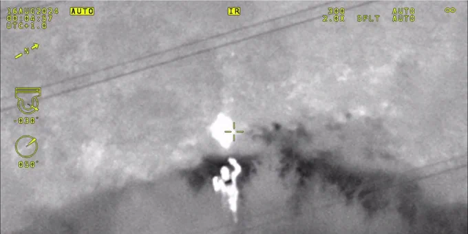 Thermal image of person in woods being approached by police officer.