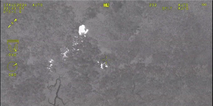 Thermal image of person in woods being approached by police officer.