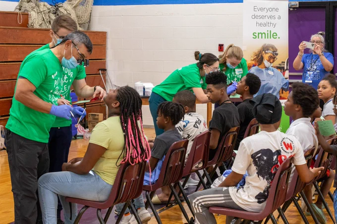 TeamSmile volunteers conduct dental screenings on children sitting in chairs with their heads leaned back. 
