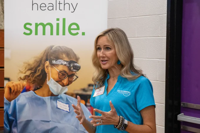 Kim Garland of the Delta Dental Foundation stands in a blue polo speaking in front of a banner. 