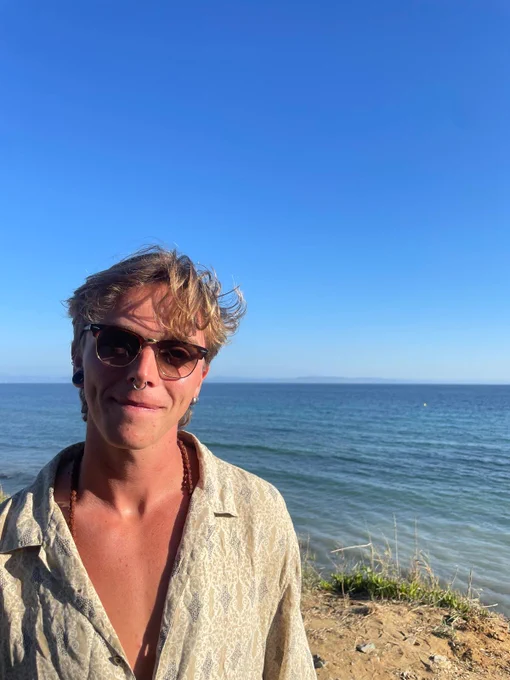 Picture of Robbie on a beach in sunglasses with blue sky and sea.