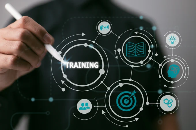 A person interacts with a digital interface displaying various icons related to training, such as a target, gears, and an open book, symbolizing a focus on education and professional development.