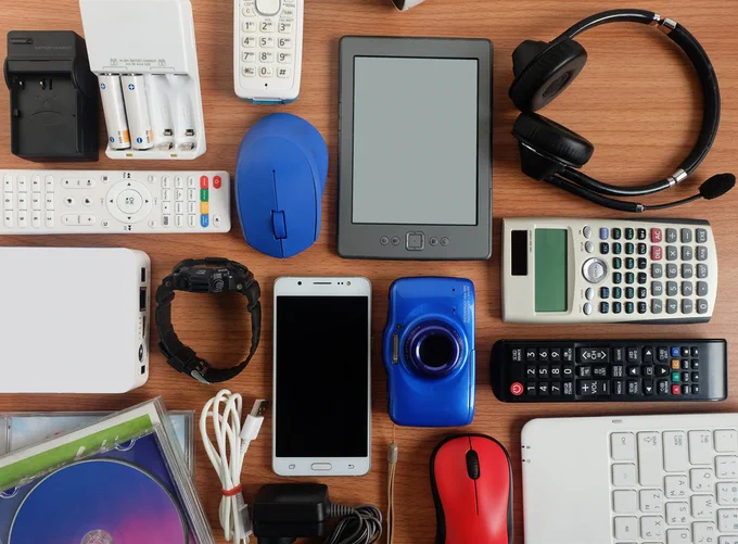 Electronics such as headphones, tablets, calculators, cameras, and cords spread across a desktop.
