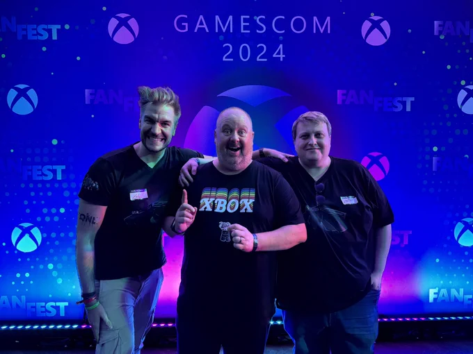 A photo taken in front of the Xbox FanFest photo wall, showing Aaron Greenberg between Loki and Leator.
Aaron points one finger upwards with raised eyebrows, suggesting an eureka moment. In the other hand he combines our Obsidian Rat sticker with our Obsidian Underpants sticker.