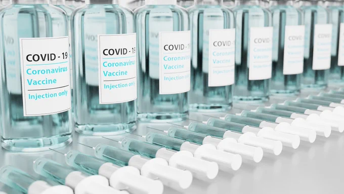 Glass phials with COVID-19 Coronavirus Vaccine are lined up above a line of syringes