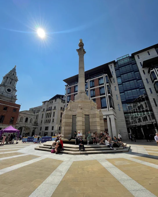 Image showing Paternoster Square Column, a neoclassical monument under a clear blue sky, surrounded by modern buildings and people sitting on its steps enjoying the sunshine.