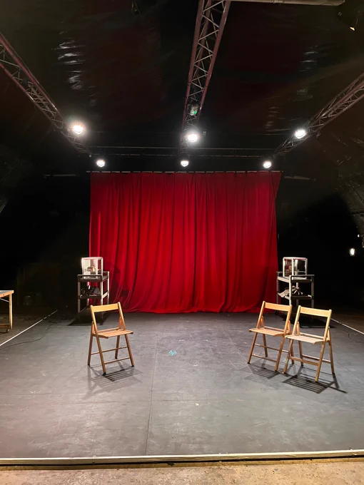 small stage, red curtain at the back three folding chairs