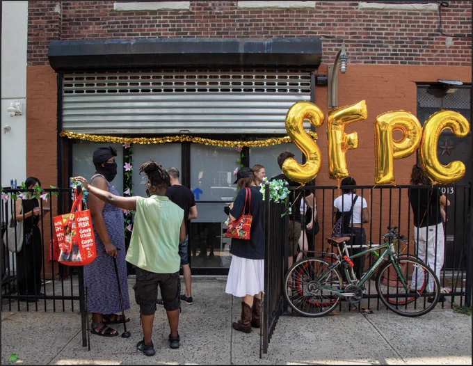 Photo of the outside of the block party's venue (LARPA). There are golden balloons that spell out SFPC, bikes, and people hanging out