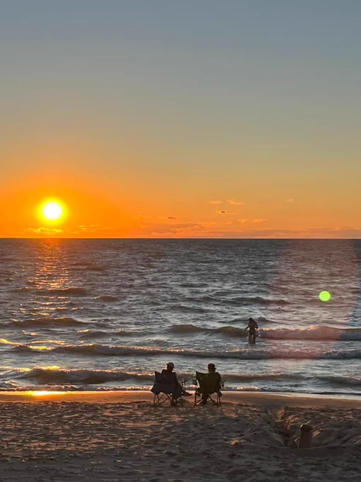 People sitting on beach and swimming as sun sets.