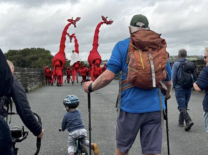 A walking group at Hewenden Viaduct being led by a performers and giant red giraffe puppets.