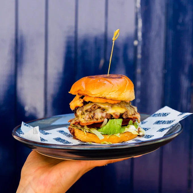 A hand holding a plate with a stacked burger on top.