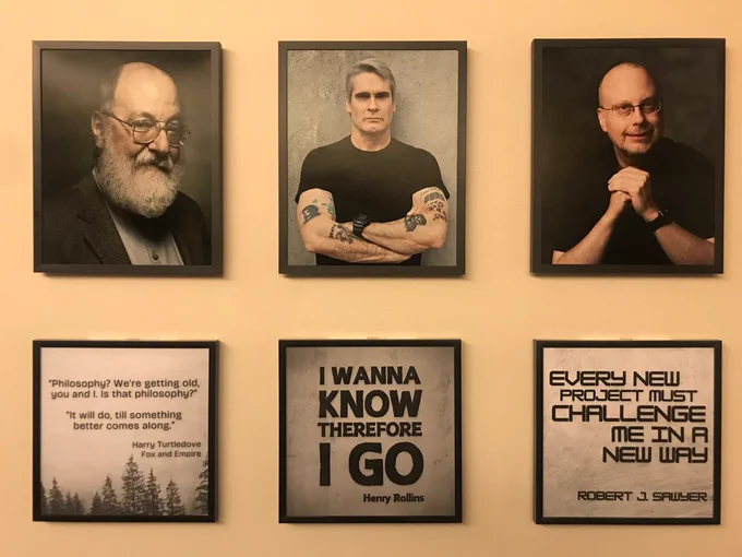 Framed photos of Harry Turtledove, Henry Rollins, and Robert J. Sawyer hang on a wall. Beneath each is a quote from their work.