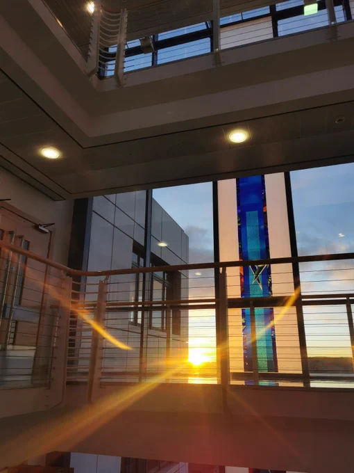 View through a window which includes a blue stained glass panel. The setting sun is shining through.