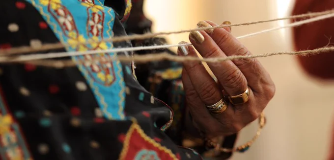 Close up of a hand, with gold rings, holding one of three pieces of string which appear horizontally across the width of the picture.