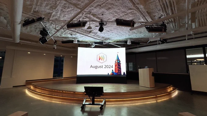 A large circular stage with a lectern and a comfort monitor with a large bright screen behind