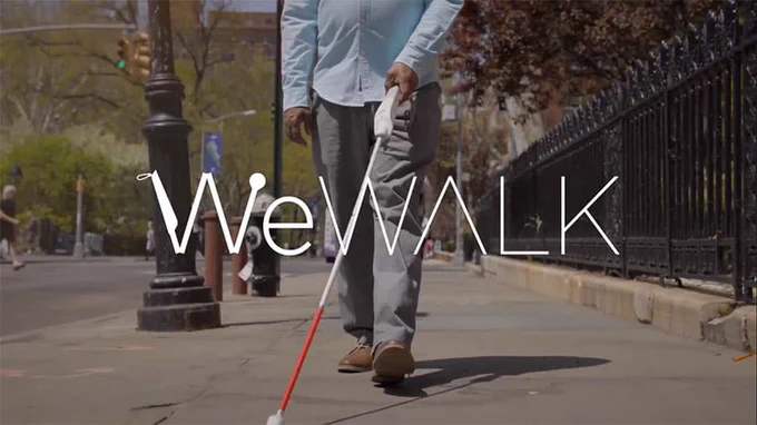 An image of a client using the WeWalk Cane 2. He is walking along the pavement with the cane in front of him.