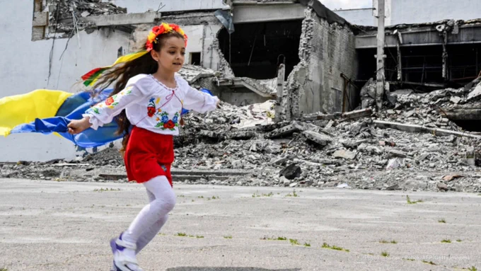 Russian missile strikes have hit thousands of schools and cultural sites in Ukraine. Above, a child runs with a Ukrainian flag during a June graduation ceremony of Kharkiv region art students. (© Sergey Bobok/AFP/Getty Images)