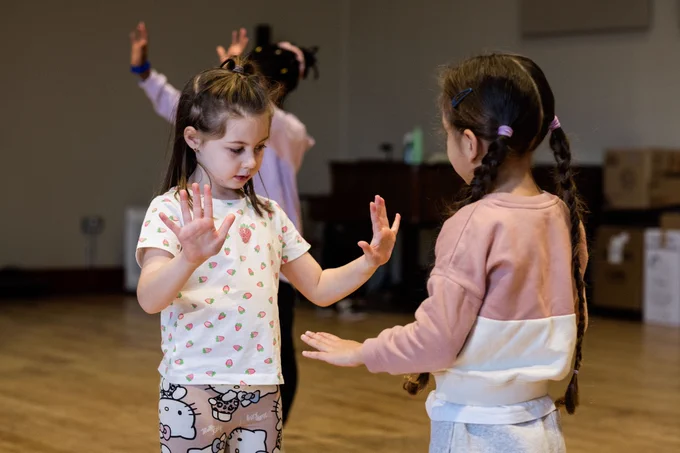 Two young children are facing each other in a mirroring game. They have their hands out in front of them. 