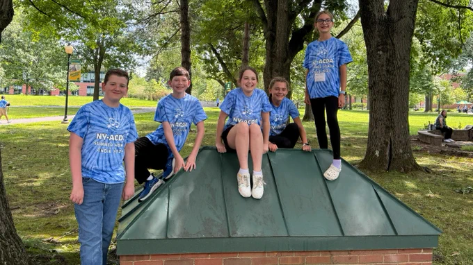 Five smiling middle school students posing in a tree filled setting.