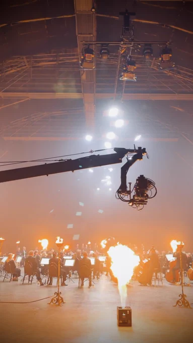 A camera jib high above a flaming pyro effect, with a symphony orchestra in the background