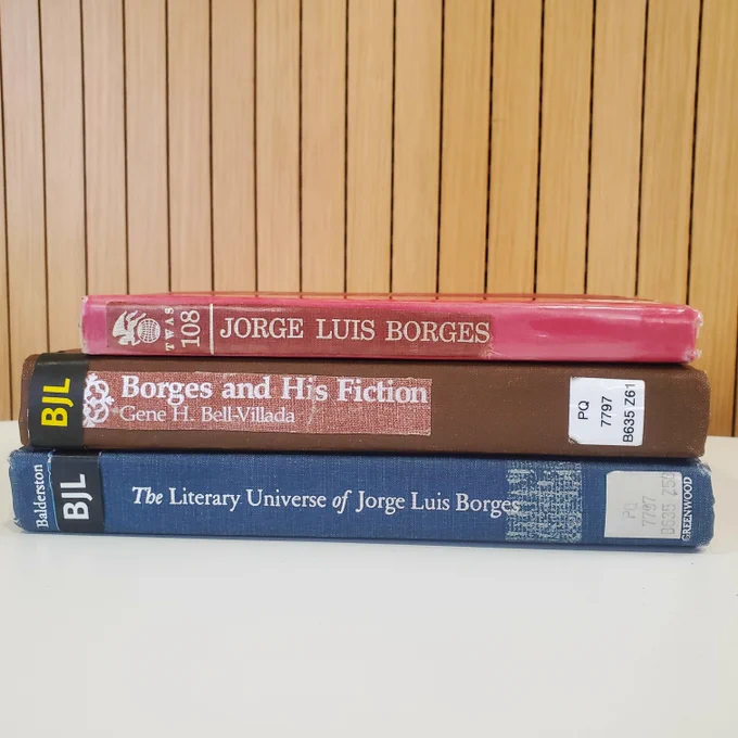 Stack of three books by Borges on a desk with wood panelling behind.