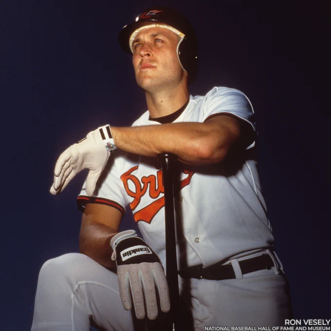 Posed portrait of Cal Ripken Jr. on one knee wearing an Orioles helmet and leaning against a bat. (Ron Vesely/National Baseball Hall of Fame and Museum)