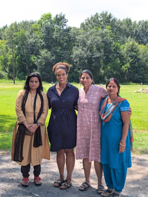 A group of four women - Farhat Jahan, Dr. Jo Banner, Rachna Dhingra, and Bati Bai Rajak - stand together in a grassy plain, smiling at the camera.