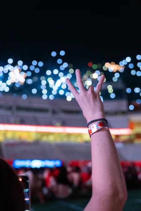 Student’s hand held up as a Cougar paw with fireworks in the background.