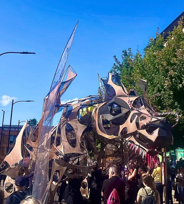 A wider view of The Hatchling dragon large-scale puppet surrounded by a crowd of people on the streets of Wakefield.