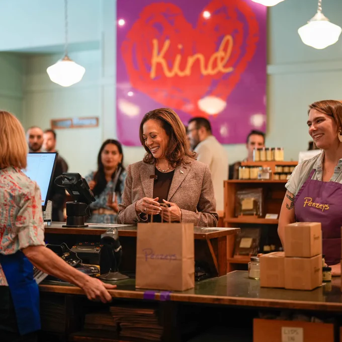 U.S. Vice President Kamala Harris smiling and interacting with a vendor at a Penzeys Spices store, with other customers and employees in the background.