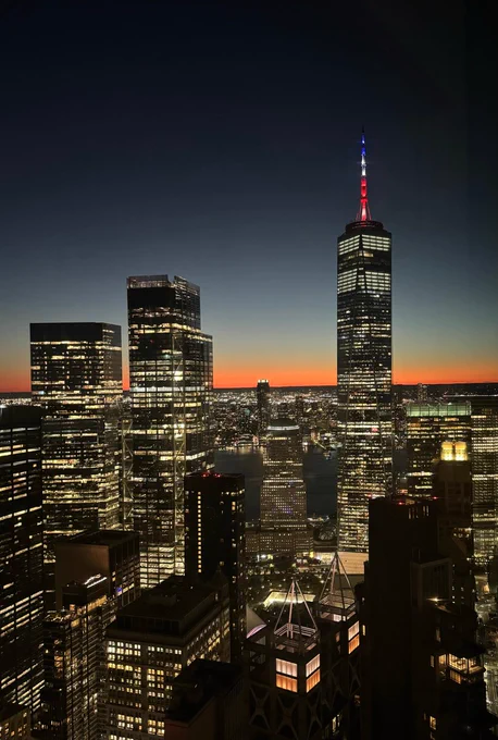 twilight view of Manhattan skyscrapers with night time lights and sun light on the horizon lowering with dark skies above